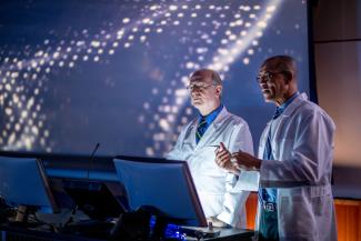 Two men in white coats looking at a computer.